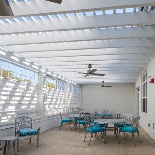 A modern outdoor patio with tables, chairs, and ceiling fans under a pergola.