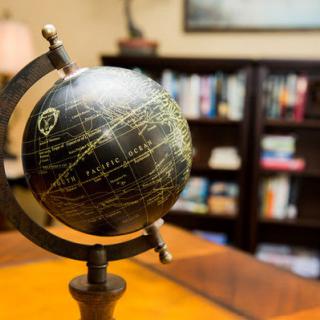 A decorative globe sits prominently on a desk in front of a well-stocked bookshelf, suggesting a scholarly or office environment.