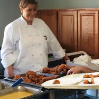 A chef in a kitchen preparing fried food on a tray.