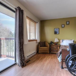 A bedroom featuring a wheelchair, with access to a balcony through sliding glass doors.