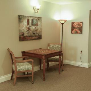 A cozy corner with a wooden table, matching chairs, a floor lamp, and framed artwork on the walls.