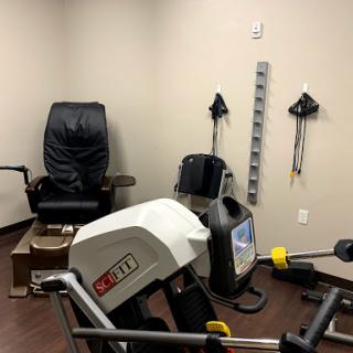 An exercise room equipped with various fitness machines and a comfortable chair for rehabilitation.