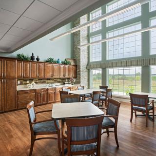 A bright dining room with large windows, wooden cabinets, and several tables and chairs.