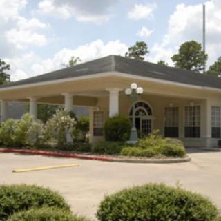 A small, well-maintained building with a covered entrance and landscaped surroundings, under a partly cloudy sky.
