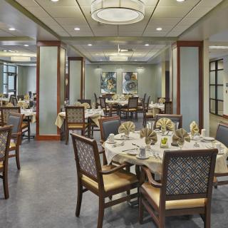 An elegant dining room with neatly arranged tables and chairs, illuminated by chandeliers.
