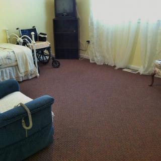A quiet living room with a wheelchair, chairs, and a window with curtains.