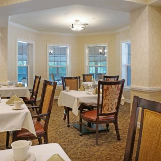 A cozy dining room with neatly arranged tables and chairs, featuring large windows and traditional decor.