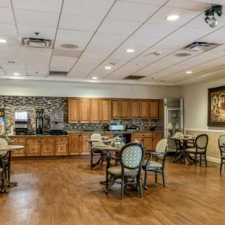A cozy dining area with wooden flooring, featuring tables and chairs, a kitchenette with cabinets, and ceiling lights.
