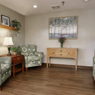 A cozy waiting room with patterned chairs, a wooden table, artwork on the wall, and soft lighting.
