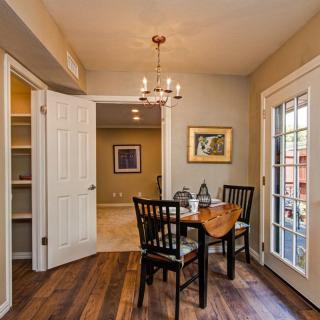A cozy dining area with a wooden table and chairs, illuminated by a chandelier, featuring glass doors that allow natural light to brighten the space.