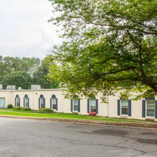 A single-story building surrounded by trees with a road in the foreground.