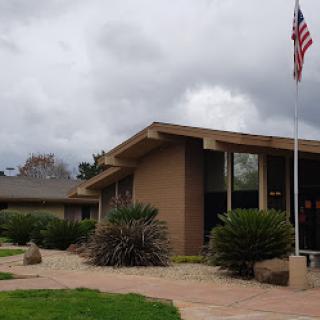 A modern building with landscaped surroundings and an American flag, set against a cloudy sky.