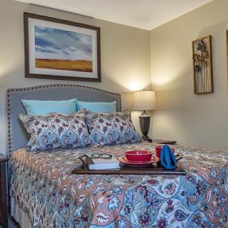 A cozy bedroom featuring patterned bedding, wall art, and a bedside lamp.