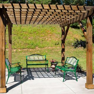 A pergola with green outdoor furniture set on a sunny patio in a garden setting.