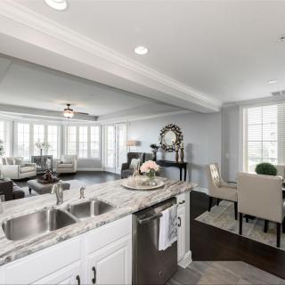 A modern, open-concept kitchen and living space with a dining area, featuring a marble countertop and ample natural light.