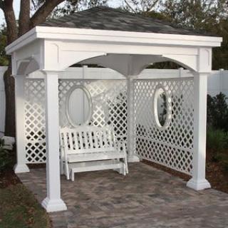 A white gazebo with lattice sides, featuring a hanging swing on a patio.