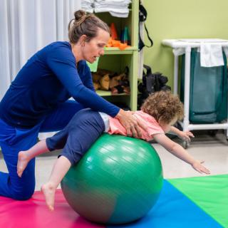 A therapist helps a child with exercises using a fitness ball for physical therapy.