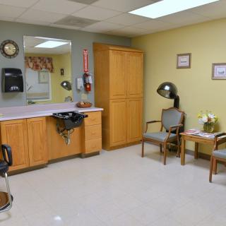 A hair salon with a waiting area featuring chairs and a hair dryer next to a counter with a mirror.