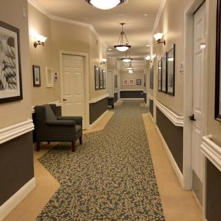 A warmly lit corridor with chairs, artwork on the walls, and patterned carpet.