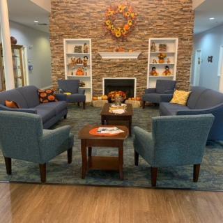 A cozy living room with a fireplace, featuring blue chairs, a coffee table, and decorative shelves.