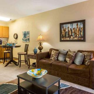 A cozy living room with a brown sofa, coffee table, and dining area, featuring elegant artwork and decorative elements.