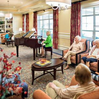 Elderly residents enjoying a social gathering in a comfortable community living room with a piano.