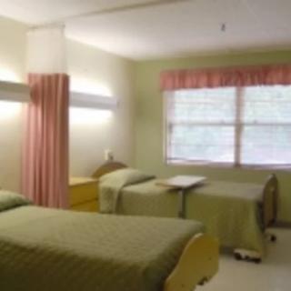 A hospital room with two beds, a curtain for privacy, and a window bringing in natural light.
