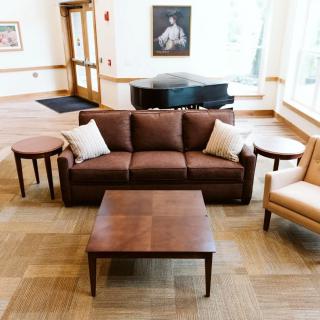 A cozy living area with a brown sofa, coffee table, and a piano in the background.