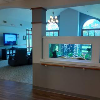 A cozy living room featuring a large aquarium built into a partition wall, with comfortable seating and a television in the background.
