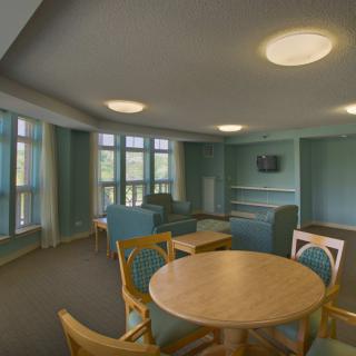 A cozy living room with a round table and chairs, soft lighting, and large windows.