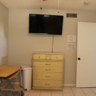A simple interior setup featuring a television, dresser, and a table in a room with tiled flooring.