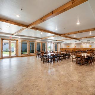 A spacious event venue featuring wooden beams and large windows that allow natural light to illuminate the dining area.