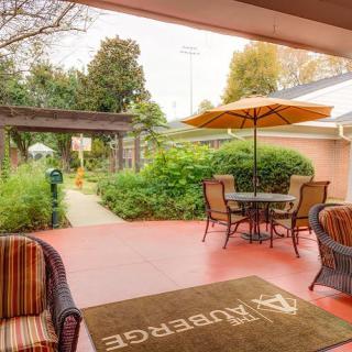 A cozy outdoor patio with table, chairs, and an umbrella surrounded by lush greenery.