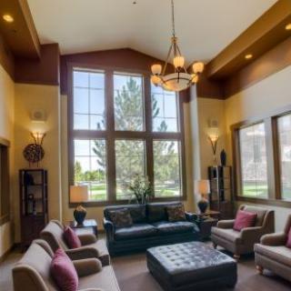 A spacious and elegantly designed living room featuring large windows, comfortable seating, and a central chandelier.