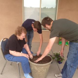 A group of people planting in a large pot together on a patio.