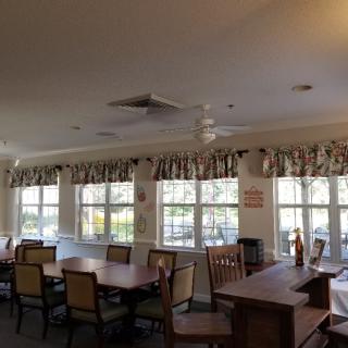 A spacious dining room with multiple tables and chairs, featuring large windows adorned with curtains.