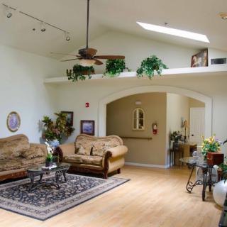 A spacious living room with neutral-toned sofas, a patterned rug, and indoor plants under skylights.