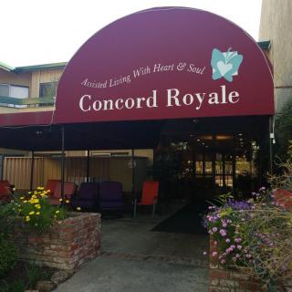 The entrance to Concord Royale is adorned with a maroon awning and surrounded by blooming flowers.