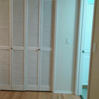 A room with wooden floors and louvered closet doors next to an open doorway.