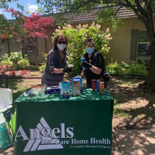 Two healthcare workers at an outdoor event promoting home health services.