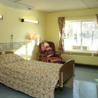 A well-lit hospital room with a single bed and a chair by the window.