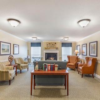 A cozy seating area with a central fireplace, featuring comfortable chairs and various decorations.
