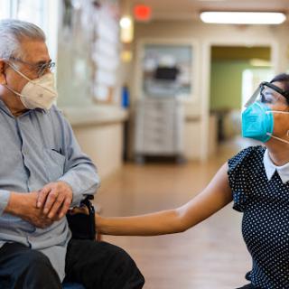 A heartfelt moment of connection between a caregiver and an elderly resident, both wearing masks for health safety.