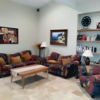 A cozy living room with colorful sofas, a wooden coffee table, and bookshelves adorned with various items.