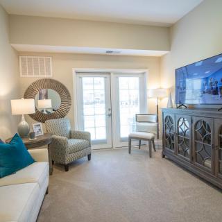A cozy living room with stylish decor, featuring a sofa, armchair, television, and elegant lighting.