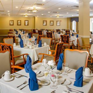 An elegantly set dining room with neatly arranged tables and chairs, featuring blue napkins.