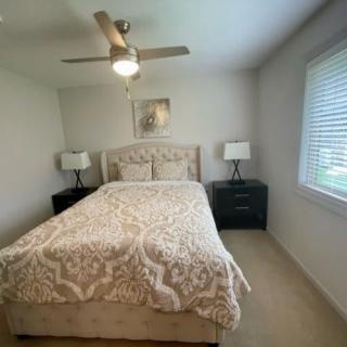 A cozy bedroom featuring a bed with patterned bedding, flanked by nightstands and lamps, and a ceiling fan above.