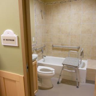 An accessible bathroom featuring a toilet, bathtub with grab bars, and a shower chair.