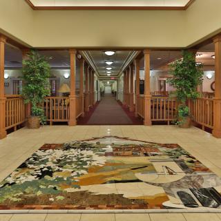 A wide hallway with wooden columns and a decorative carpet, flanked by potted plants.
