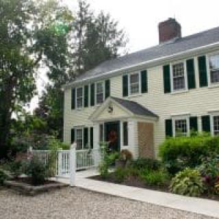 A charming colonial-style house with a manicured garden and a gravel pathway.